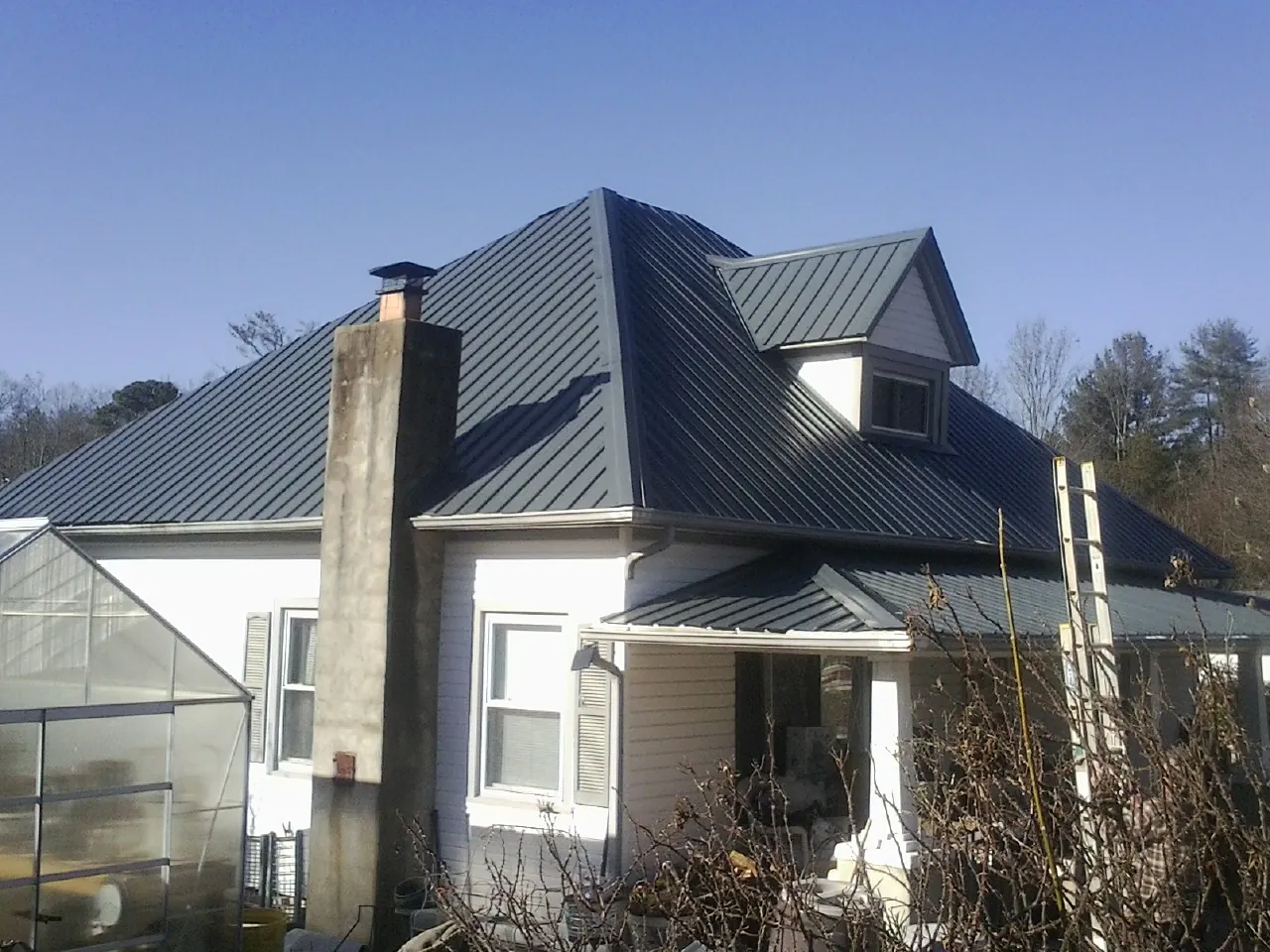 Dark blue standing seam metal roof on a white farmhouse with dormer — Slate & Tile Roof Repair by Roofing Brothers in Pella