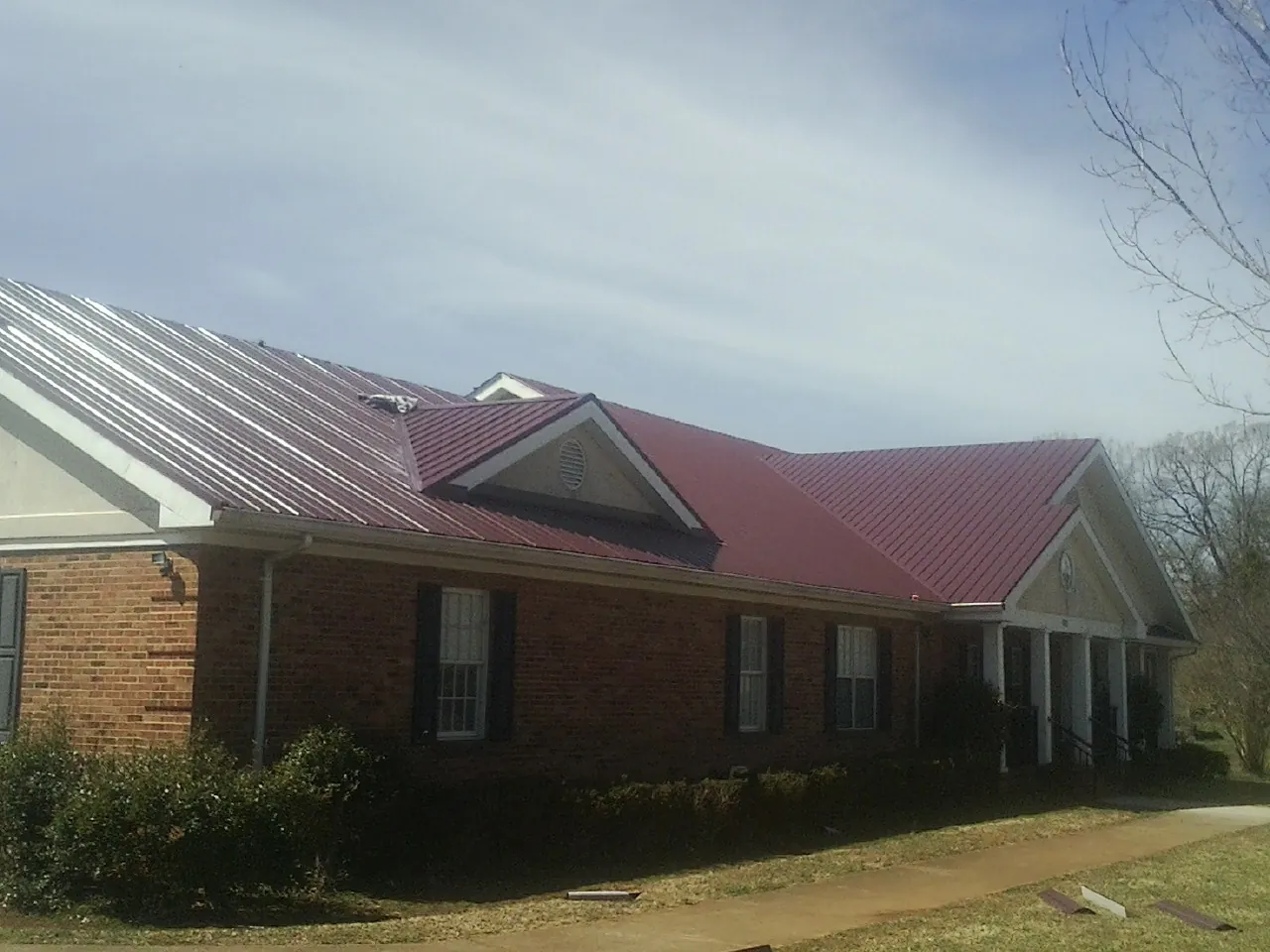 Red metal roof with gabled entries on a long brick building, from a Hail Damage Roof Repair job in Pella