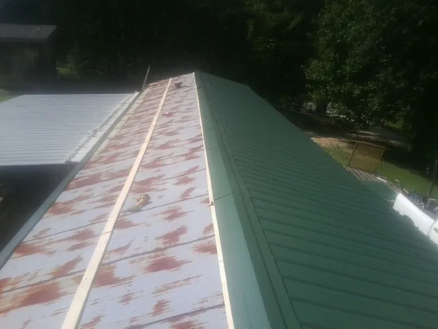 Old rusted panels beside newly installed green metal roofing — Wind Damage Roof Repair by Roofing Brothers in Pella