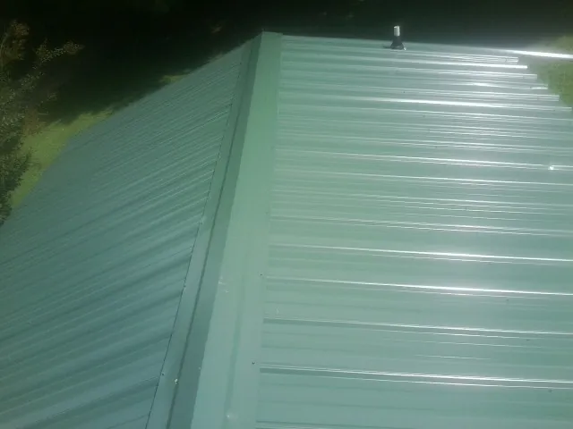 New green metal panels meeting at the ridge of a roof — Flat Roof Repair work by our crew in Pella