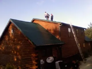 Crew on the ridge of a green metal roof on a two story log home in Pella