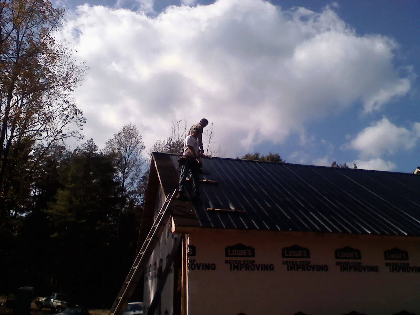 Roofer fastening dark metal panels high against a cloudy sky, from a Roof Inspection job in Pella