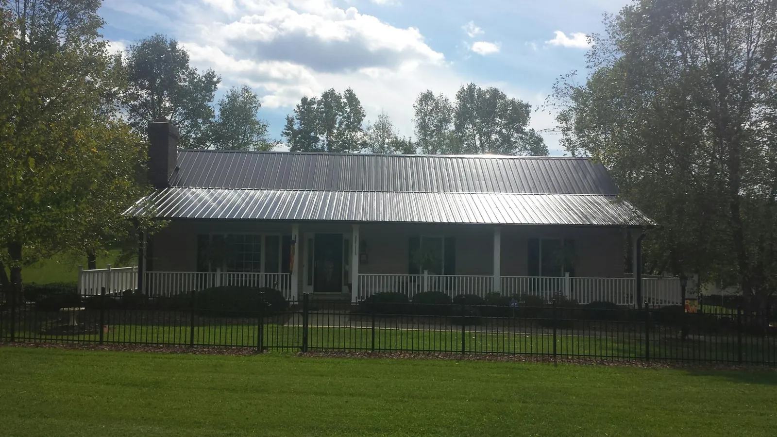 Gray metal roof on a brick ranch with a full width front porch — Gutter Guard Installation work by our crew in Pella