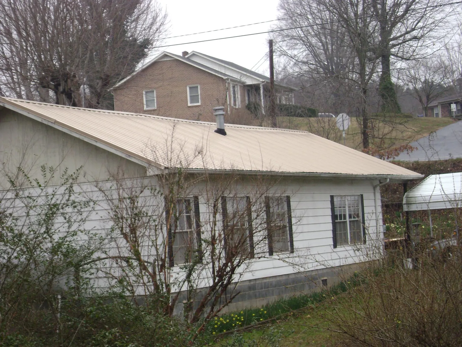 Tan metal roof on a white sided house set into a hillside — Commercial Roofing by Roofing Brothers in Pella