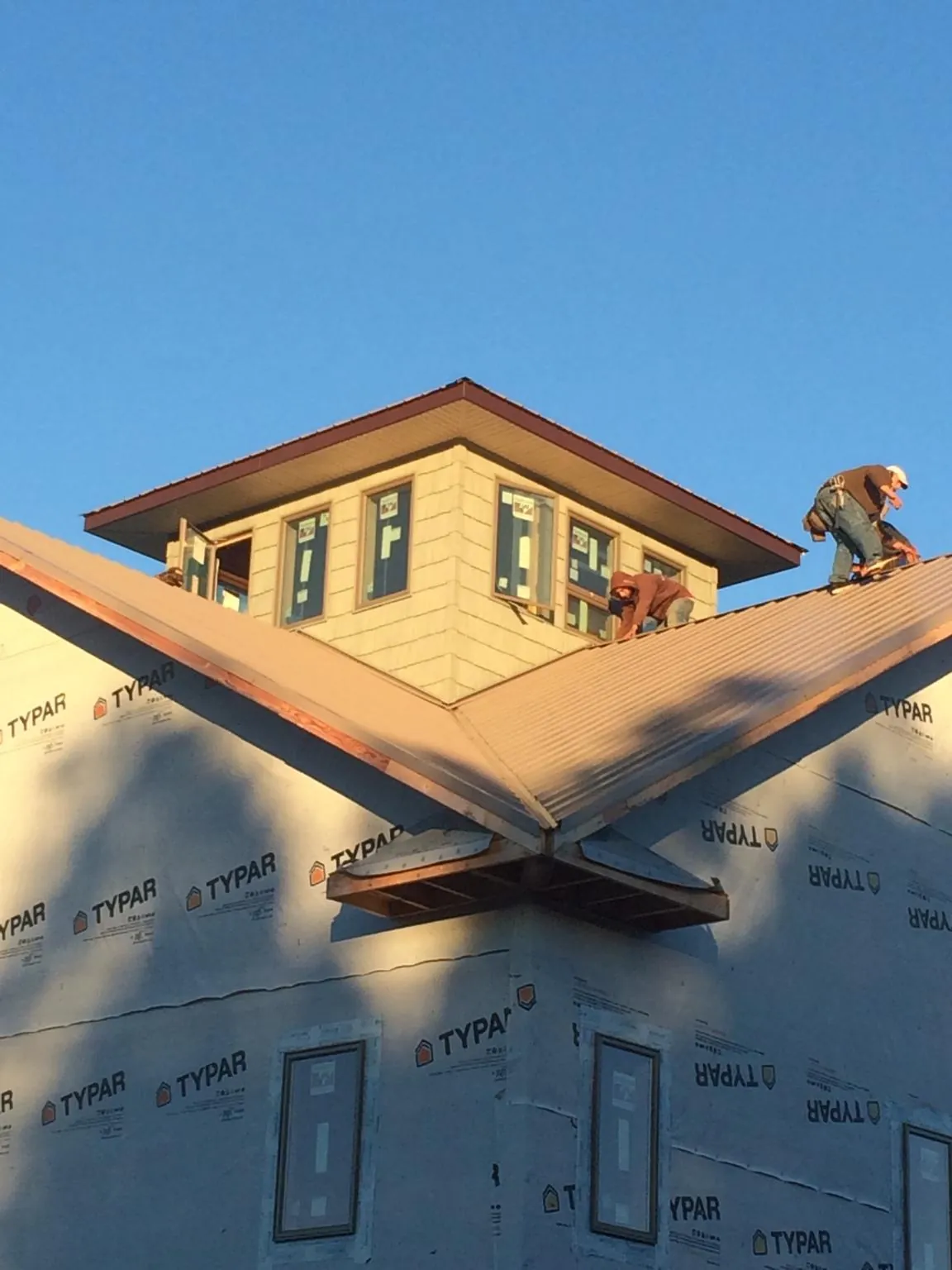 Roofers working around a rooftop cupola on a new metal roof at sunset — Roof Waterproofing in Pella by Roofing Brothers